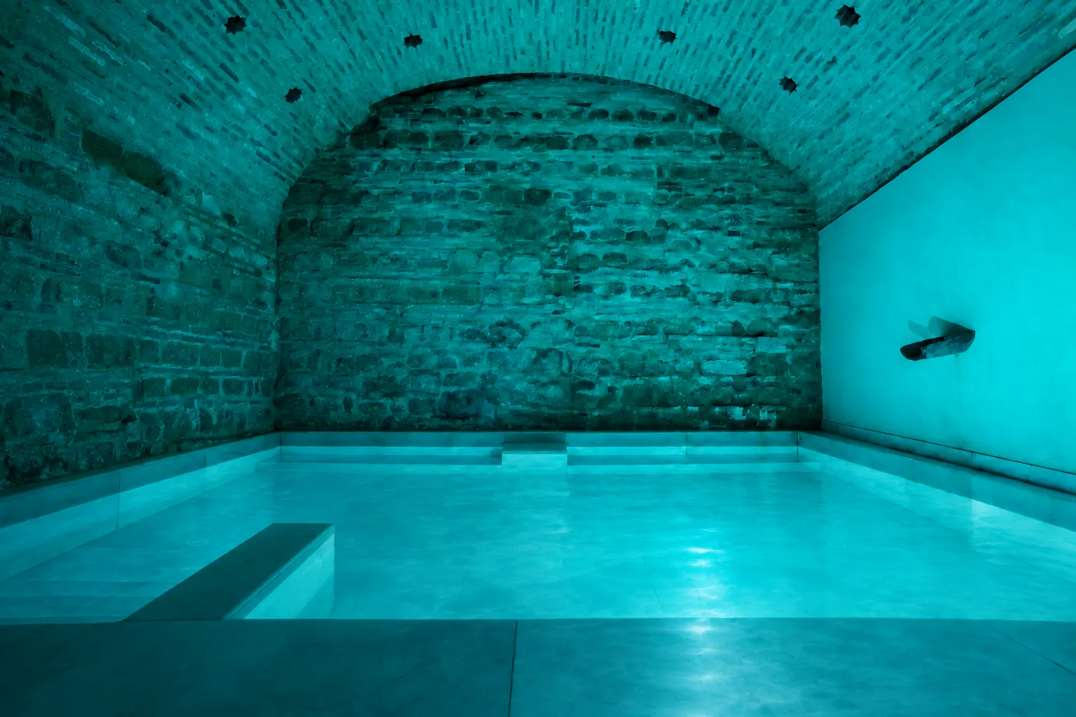 Piscina turquesa del hammam bajo una bóveda de ladrillo en los Baños Árabes de Córdoba